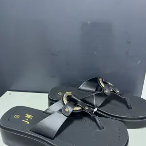 black wedge platform and distinctive gold-tone metal hardware on the T-strap