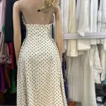 Vintage-inspired polka dot halter-neck maxi dress with black polka dots, a plunging neckline, and a contrasting black bow or ribbon accent at the bust.