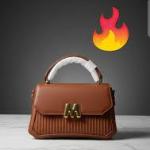 Identified by its gold M-shaped embellishment is a designer-inspired crossbody bag